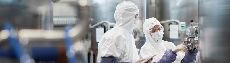  Two workers wearing protective suits while using equipment at modern chemical plant